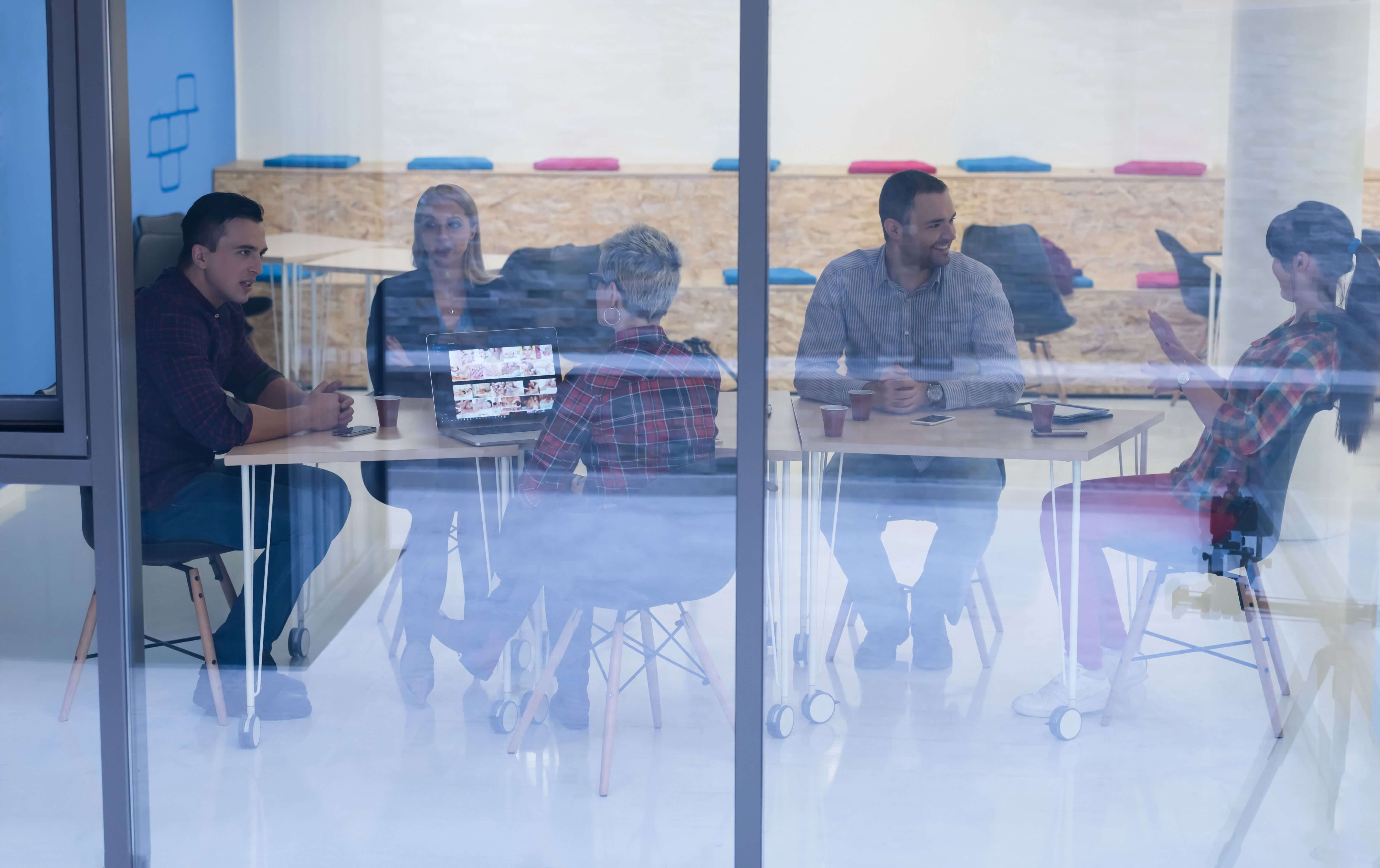 A group of people in a business meeting shown behind transparent glass.
